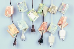 Electric power plugs with Euro banknotes on them hanging on light blue background. Energy efficiency, power consumption, electricity cost, and expensive energy concept