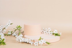 Geometric podium platform stand for product presentation and spring flowering tree branch with white flowers on pastel beige background. Front view