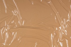 Crumpled wrinkled plastic transparent plastic cellophane on pastel brown color background. Abstract creative texture background