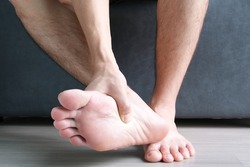 Toe pain man sitting on sofa and he grabs a toe that's inflamed from osteoarthritis . Health concepts.