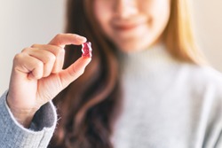 Closeup image of a beautiful woman holding and looking at a red jelly gummy bear 