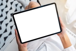 Top view mockup image of a woman holding black tablet pc with blank white desktop screen while sitting in bedroom with feeling relaxed in the morning