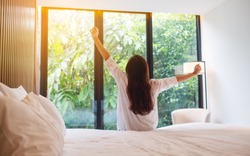 Rear view image of a woman do stretching after waking up in the morning  , looking at a beautiful nature view outside bedroom window 