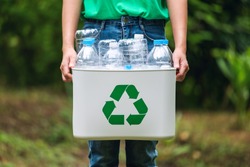 A woman holding a recycle bin with plastic bottles in the outdoors