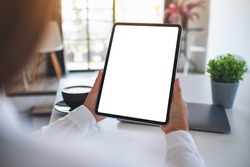 Mockup image of a woman holding digital tablet with blank white desktop screen with coffee cup on the table