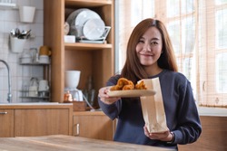 A beautiful young asian woman holding a plate of fried chicken and paper food bag at home for food delivery concept