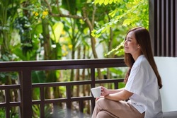 Portrait image of a beautiful young asian woman drinking coffee and relaxing while sitting on balcony at home
