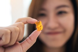 Closeup image of a beautiful Asian woman smiling , holding and looking at orange gummy bear 
