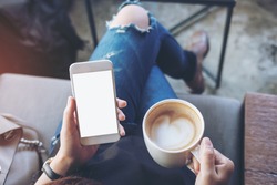 Mockup image of woman's hands holding white mobile phone with blank screen on thigh and coffee cup in cafe