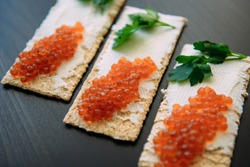 Red caviar on crispy bread with cream cheese and green. Healthy food. Sandwiches with caviar isolated on black background, selective focus.