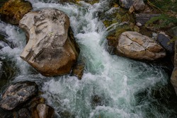 Rapid and powerful water flow between large rocks, close-up. Boulders in cold mountain river. Natural backgrounds.