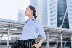 A beautiful Asian business woman is standing in a business district and looking ahead for something.