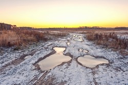 On an autumn morning, puddles on the road are covered with ice and snow.