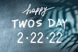 Happy Twos Day 2.22.22 vector concept. White chalk lettering on scholboard background with palm leaves shadows. February 2nd, 2022 is such an significant date.