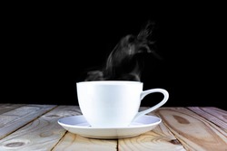White cup hot drinking with steam on pine wooden table over black background.