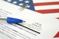 I-9 Employment Eligibility Verification blank form lies on United States flag with blue pen from Department of Homeland Security
