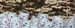 US dollar bills on fabric with texture of Ukrainian military pixeled camouflage. Cloth with camo pattern in grey, brown and green pixel shapes. Official uniform of Ukrainian soldiers close up