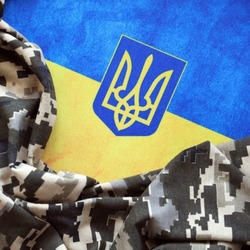 Ukrainian flag and coat of arms with fabric with texture of pixeled camouflage. Cloth with camo pattern in grey, brown and green pixel shapes with Ukrainian trident sign close up.