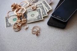 Many expensive golden jewerly rings, earrings and necklaces with big amount of US dollar bills close to smartphones. Pawn shop concept