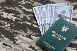 Ukrainian military ID and US dollar bills on fabric with texture of pixeled camouflage. Cloth with camo pattern in grey, brown and green pixel shapes with Ukrainian army personal token close up.