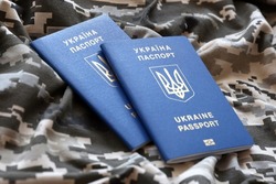 Ukrainian foreign passport on fabric with texture of military pixeled camouflage. Cloth with camo pattern in grey, brown and green pixel shapes and Ukrainian ID close up