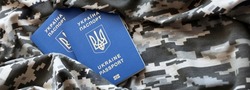 Ukrainian foreign passport on fabric with texture of military pixeled camouflage. Cloth with camo pattern in grey, brown and green pixel shapes and Ukrainian ID close up