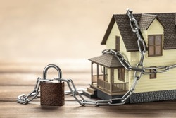 House tied with a chain and a closed lock. The concept of a ban on the sale of real estate, house arrest.