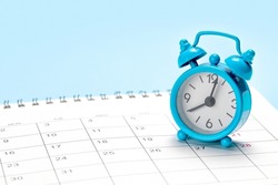 Blue alarm clock on a calendar with a blue background.