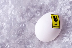 Delivery of fragile goods in the package. Egg with a sticker with a symbol of a glass with a crack and an inscription fragile in a film with air pads.