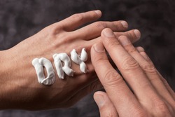 The word Dry is written in cream. Dry hands of a man in cream or ointment. Gray background