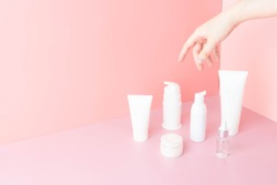 Skincare routine- Women hand choosing skin care products for healthy skin on pink background. Packaging of facial foam, cleansing, essence, serum, cream/lotion. Beauty and cosmetic concept. Minimal.
