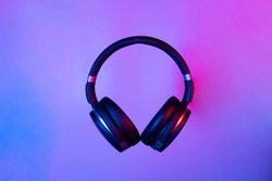 Black wireless bluetooth headphones on neon light background. Music concept.