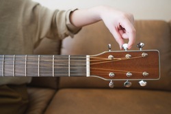 Woman hands tuning acoustic guitar strings before playing music lesson at home. Close up.