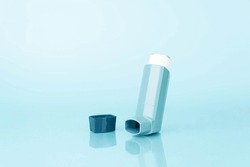 Asthma inhaler with reflection on blue background. Pharmaceutical product contains bronchodilator for treat or prevent asthma attack. World Asthma Day.