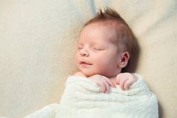 Smiling newborn baby with Mohawk hair sleeping in white blanket.