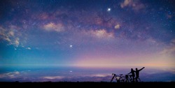 Silhouette Couple cycling on Panorama blue night sky milky way and star on dark background.Universe filled with stars, nebula and galaxy with noise and grain.
