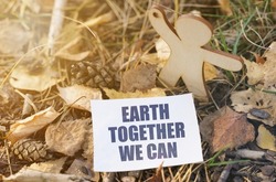 Ecology. On the ground among the leaves near the wooden figure of a man paper with the inscription - Earth Together We Can