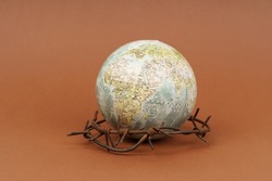 The concept of symbolism. On a brown surface is a globe, which is surrounded by barbed wire.