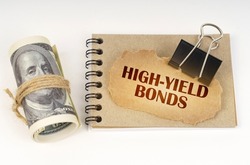 Business and finance concept. On a white surface are twisted dollars, a notebook and a cardboard sign with the inscription - High-Yield Bonds