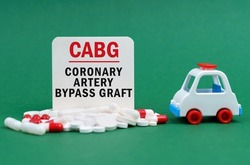 Medical concept. On a green surface, an ambulance, pills and a white sign with the inscription - Coronary artery bypass graft