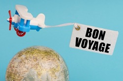 Travel and business concept. On a blue background, a globe and an airplane with a sign - Bon voyage. Globe out of focus.