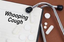 Medical concept. On a brown surface lies a stethoscope, pills and a notepad with the inscription - Whooping Cough