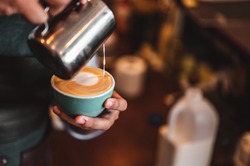 Close-up of professionally extracting coffee by barista with a pouring steamed milk into coffee cup making beautiful latte art. coffee, extraction, deep, cup, art, barista concept. 