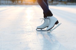 Closeup of  female legs in white old fashion skates on outdoor ice rink. Young woman skating on frozen lake in snowy winter park on sunset time