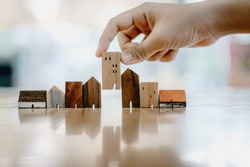 Hand choosing mini wood house model from model and row of coin money on wood table, selective focus, Planning to buy property. Choose what's the best. A symbol for construction ,ecology, loan concepts