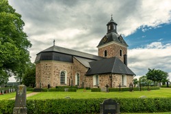 Beautiful old church located in St.Skedvi in Sweden, and a well cared cemetery with rows of gravestones and colorful flowers. On a beautiful summer day with lush green trees, sunlight and a blue sky
