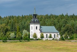 Beautiful view of a white church on the Swedish countryside with a green forest in the back and bright summer sunlight