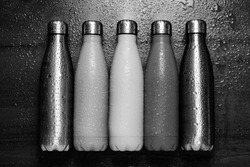 Stainless thermos bottles on a wooden table sprayed with water. Black and white.