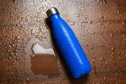 Stainless steel thermos bottle isolated on a wooden table sprayed with water. Blue color.