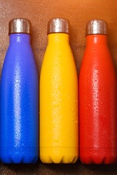 Colorful stainless thermo bottles, on a wooden table sprayed with water.